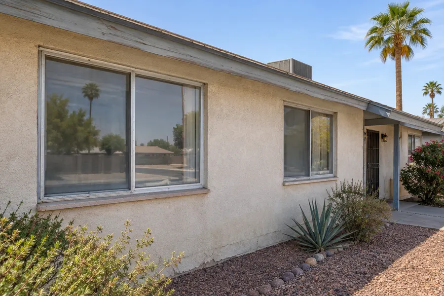 Exterior of an older single-story Tempe stucco home with tired original single-pane aluminum slider windows, oxidized silver frames, faded weather stripping and a sun-bleached wall